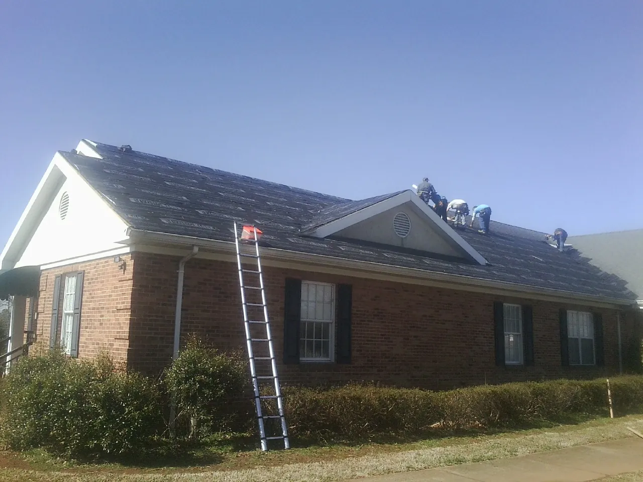 Crew tearing shingles off a brick ranch roof with a ladder set — Metal Roof Repair work by our crew in Shelby